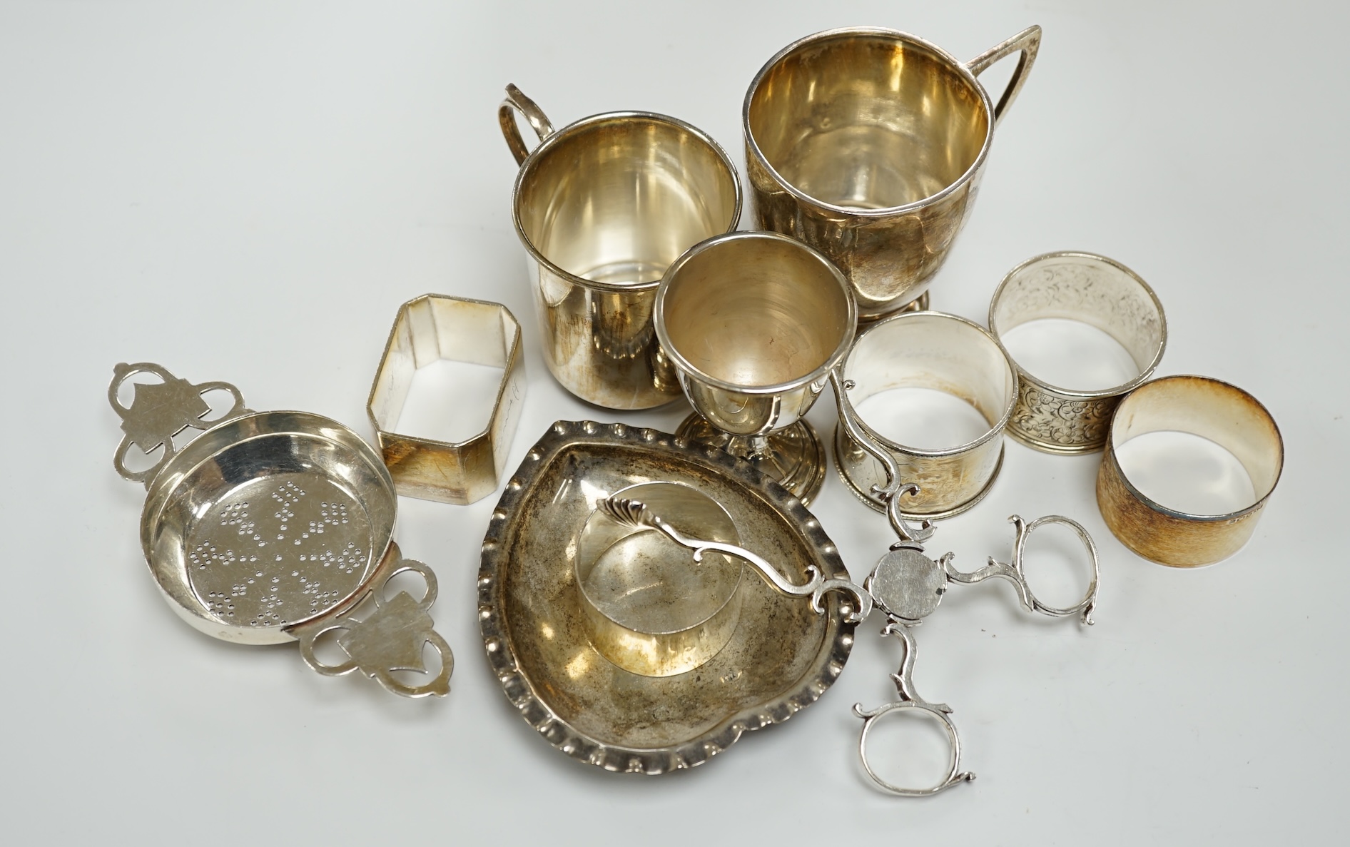 Assorted small silverwares including napkin rings, mugs, tea strainer and pair of Georgian sugar nips.